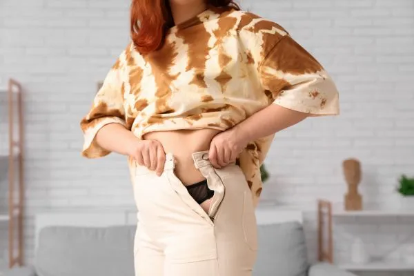 Image of woman trying to do her trousers up after pregnancy weight gain Cumbernauld