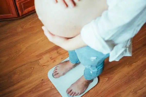 Image of woman weighing herself and experiencing weight gain through pregnancy Cumbernauld
